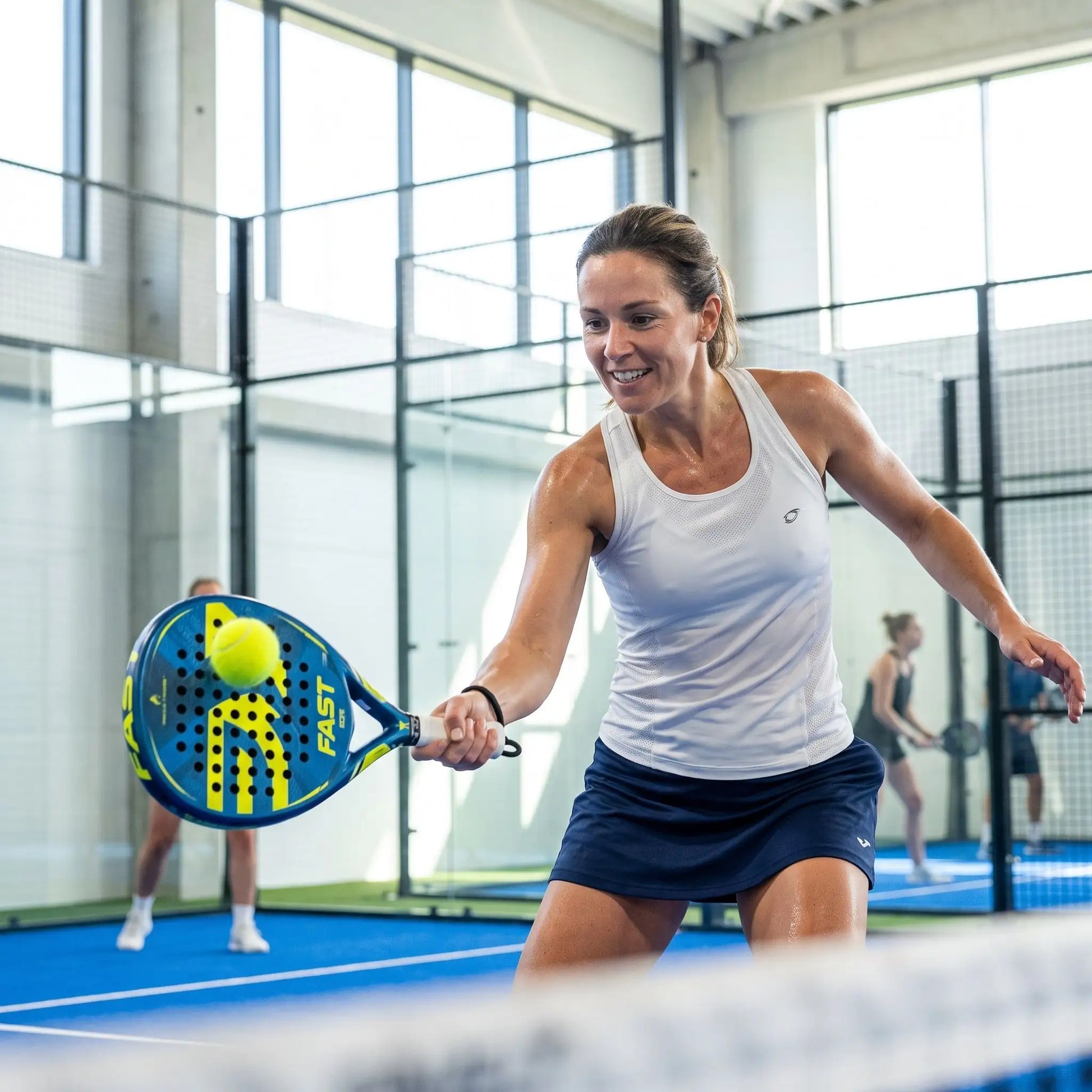 Femme frappe une balle sur terrain intérieur avec raquettes padel